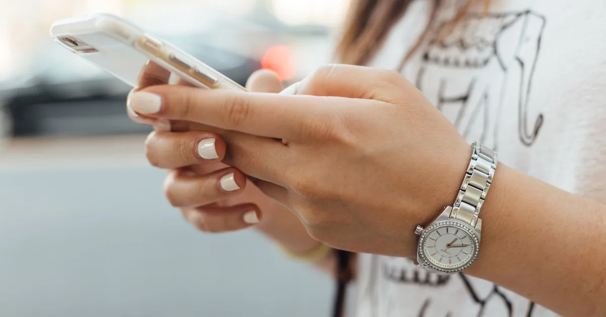 A woman with white nail polish texting on her iPhone.