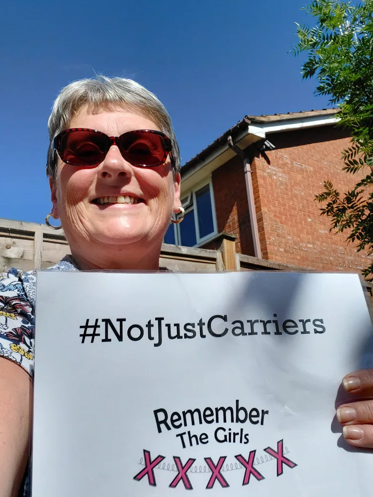 A woman in sunglasses holding up a sign that reads "#NotJustCarriers" above the Remember The Girls logo.