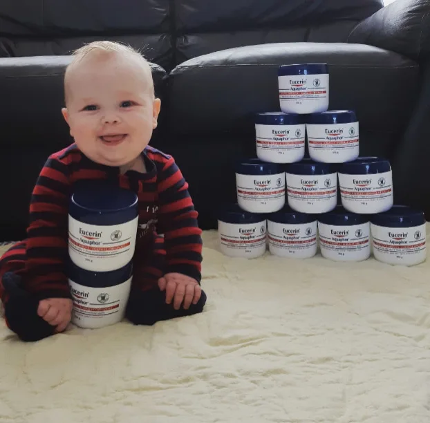 A baby behind and next to Eucerin Aquaphor containers.