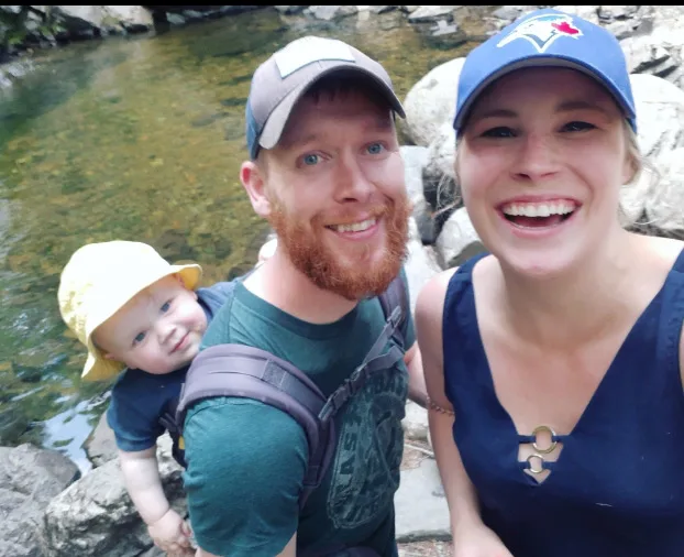 A mother, father, and a baby on a hike near a river.