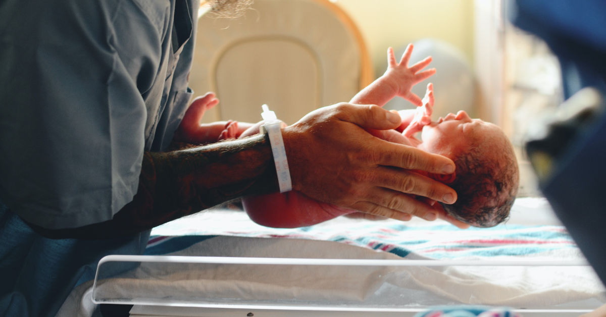 A nurse placing a newborn baby on a scale.