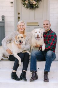A lovely couple posing for a photo with their two dogs sitting on a door step.