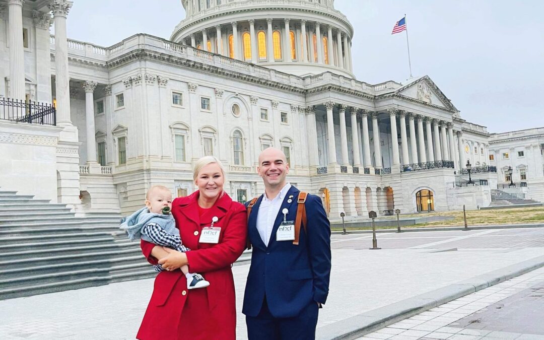 Young couple standing in front of the white house with their new born child.