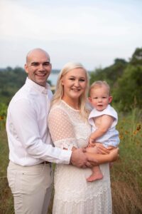 Young couple posing together with their child in a field of flowers.